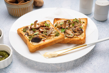 Plate of tasty toasts with cream cheese, mushrooms and pesto sauce on light table, closeup