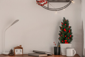 Workplace with small Christmas tree and calendar near light wall