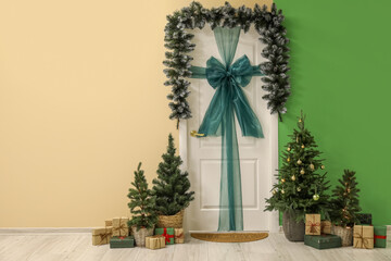 White door with bow, Christmas branches, fir trees and presents in hall