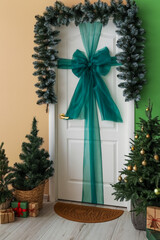 White door with bow, Christmas branches, fir trees and presents in hall