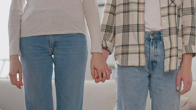 Lesbians stands next to each other holding hands tenderly