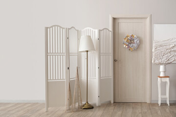 Interior of light room with wooden door, Christmas wreath and folding screen