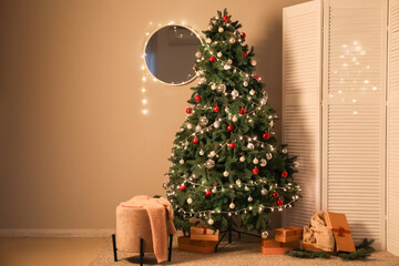 Interior of living room with glowing Christmas tree, pouf and folding screen at night