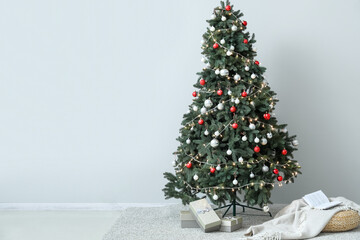 Glowing Christmas tree with presents and pouf near light wall