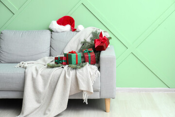 Sofa with Santa hat, Christmas branches and presents near green wall