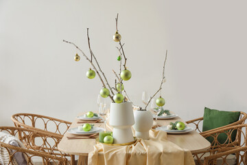 Vases with tree branches and green Christmas balls on dining table near grey wall
