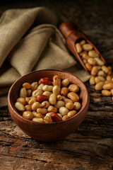 Old and rusty wooden table with a wooden bowl with shelled peanuts and some peanuts and in the wooden ladle, selective focus