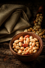 

Old and rusty wooden table with a wooden bowl with shelled peanuts and some peanuts and in the wooden ladle, selective focus