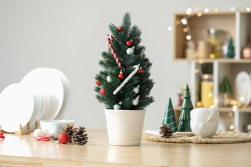 Small Christmas tree with toys and fir cones on table in kitchen