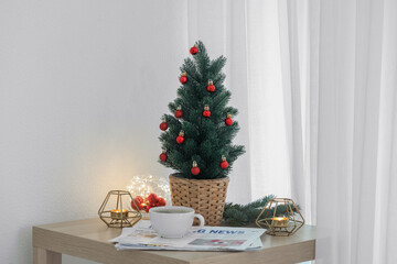 Small Christmas tree, coffee cup, newspapers and candles on table in living room