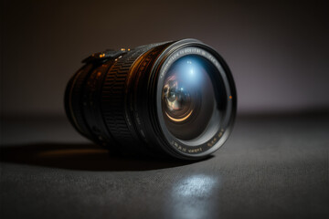 Camera lens sits on a dark table under a spotlight tech review - obrazy, fototapety, plakaty