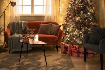Interior of dark living room with glowing Christmas tree, sofa and armchair