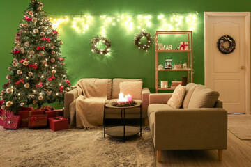 Interior of dark living room with glowing Christmas tree, wreaths and sofas