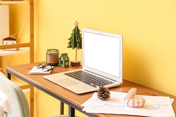 Laptop with Christmas toys and candle on table near yellow wall in office