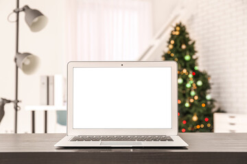 Fototapeta premium Laptop on table against blurred Christmas tree in office
