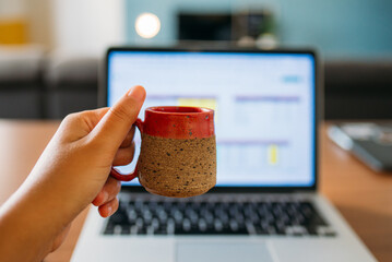 Mulher segurando xícara em frente ao computador enquanto trabalha