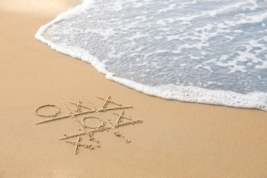 Tic tac toe game drawn on sand near sea, space for text