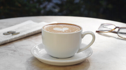 Cup of delicious coffee, glasses and newspaper on beige marble table outdoors