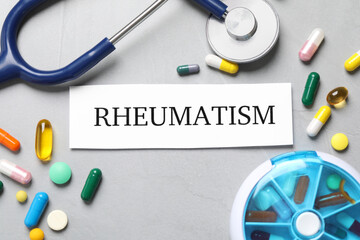 Sheet of paper with word Rheumatism, stethoscope and many different pills on light grey table, flat...