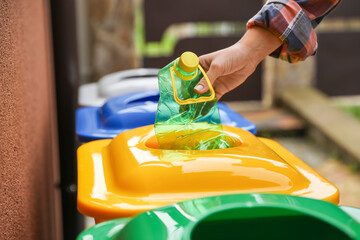 Woman throwing plastic bottle into recycling bin outdoors, closeup