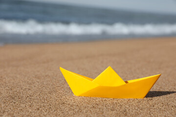 Fototapeta na wymiar Yellow paper boat near sea on sandy beach, space for text