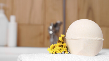 Towel with bath bomb and flowers on tub indoors, closeup. Space for text