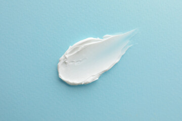 Sample facial cream on turquoise background, top view