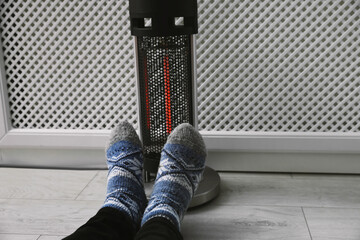 Man warming feet near modern heater indoors, closeup