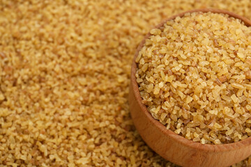 Wooden bowl on pile of uncooked bulgur, closeup. Space for text