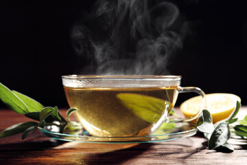 Cup of aromatic herbal tea and fresh sage on wooden table