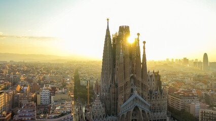 Closeup aerial view of the Sagrada Familia cathedral in Barcelona, Spain. Cathedral is in shadow with the sun rising behind cathedral between two spires.