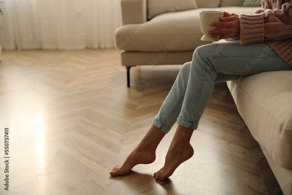 Poster Barefoot woman sitting on sofa in living room, closeup. Floor heating system