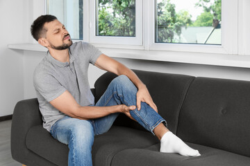 Man suffering from pain in leg on sofa at home