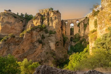 Wall murals Ronda Puente Nuevo Daytime panoramic image of the clifftop village of Ronda, in Andalucia, Spain, at sunset. The Puente Nuevo bridge and cliffs are bathed in golden light.