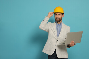 Professional engineer in hard hat with laptop on light blue background, space for text