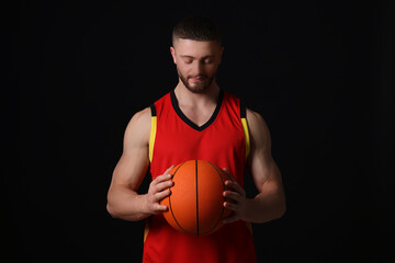 Athletic young man with basketball ball on black background