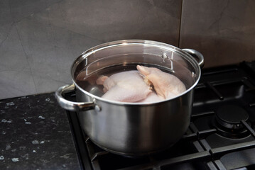 Stalowy garnek na kuchence gazowej, ćwiartki z kurczaka zalane wodą