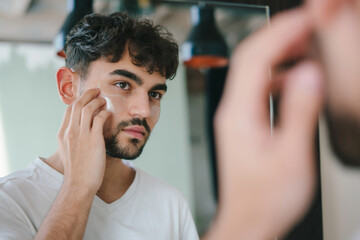 Bearded man applying eye patches under his eyes while looking at mirror. Wrinkles and face home...