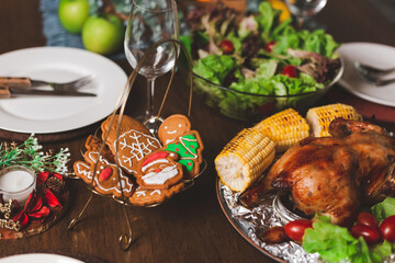 Fototapeta na wymiar Traditional celebration. Roasted chicken, wine, vegetables salad and various food are set on table for family to celebrate together at night and Christmas tree set in the room for Christmas holiday.