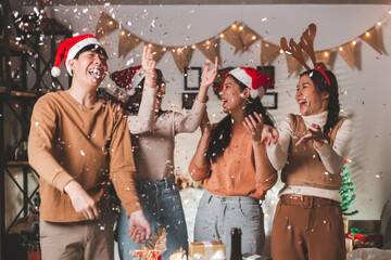 Group of young adult Asian friends enjoying Christmas eve party and blowing confetti at home with...