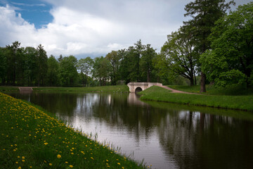 Fototapeta na wymiar View of the Karpin Bridge on the shore of the pond in Gatchina Park on a sunny summer day, Gatchina, St. Petersburg, Russia