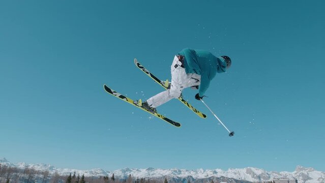 VOGEL, BOHINJ, JULIAN ALPS, SLOVENIA, MARCH 2022: SLOW MOTION: Amazing view of following freestyle skier jumping on big air kicker. Extreme athlete rotating through the air and performing grab trick.