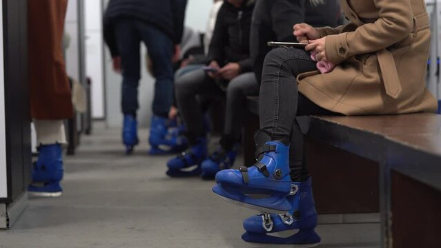 People Wearing Ice Skating Shoes Sitting On Bench At The Ice Rink. - crop shot