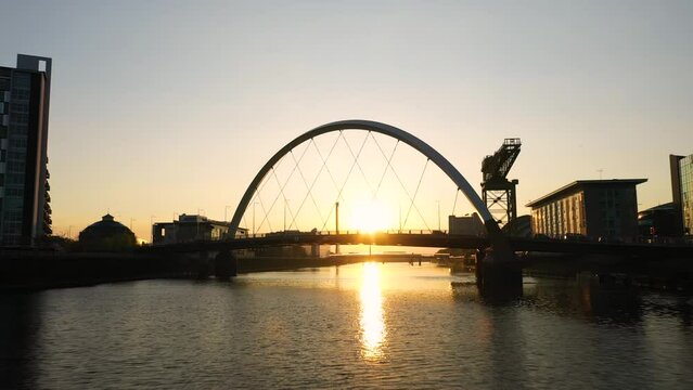 Drone shot flying underneath the Squinty Bridge (Glasgow Arc) along the Clyde River in Glasgow at sunset