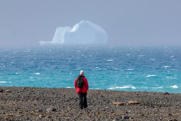 Papier Peint photo autocollant Antarctique A traveller to Antarctica walks a remote beach as massive icebergs float by in the crystal clear water