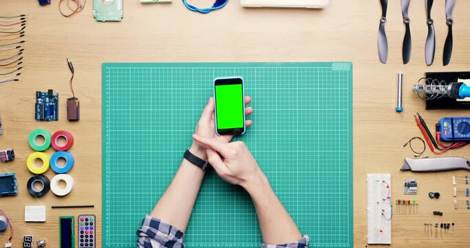 Technician, hands and scroll on green screen phone with tools on desk for engineering, computer or hardware. Engineer, programmer and mockup top view for app, website or smartphone at workshop table