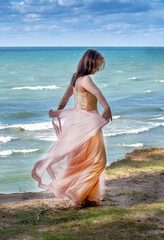 pretty  young  lady in a flowing peach dress, walks along a ledge high over Lake Michigan USA