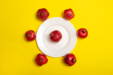 Seven ripe red pomegranates on a white plate on a yellow background