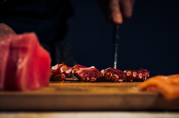 Close up of Chef cook hands chopping octopus for traditional Asian cuisine with Japanese knife. Professional Sushi chef cutting seafood japanese chefs are making octopus sashimi. Dark Tone