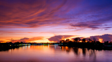 Dramatic dusk sky over the riverbank with colorful majestic orange sunlight clouds after sundown